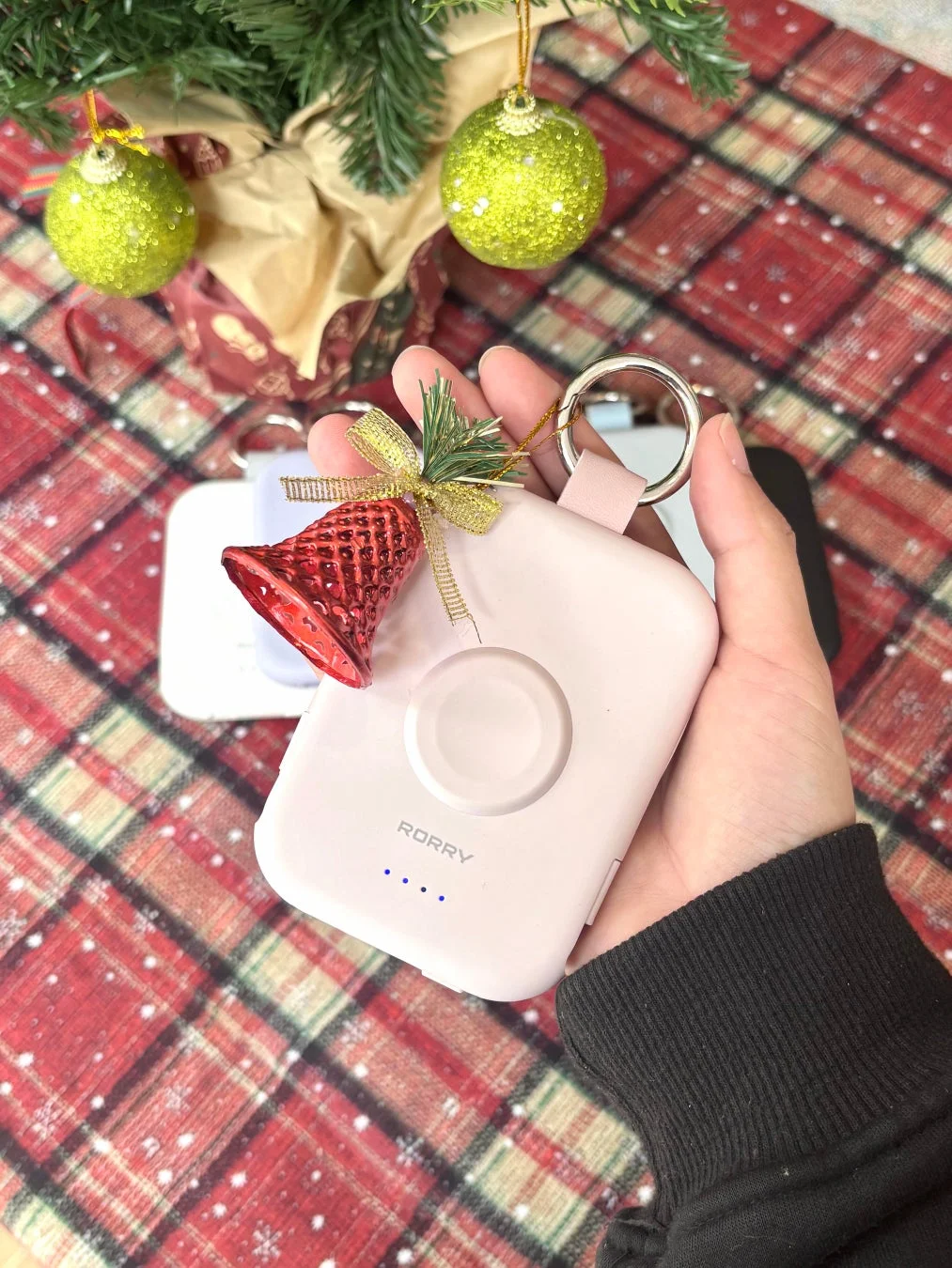 クリスマスツリーとチェック柄の背景を背に、手がピンク色のポータブル充電器を持っている様子