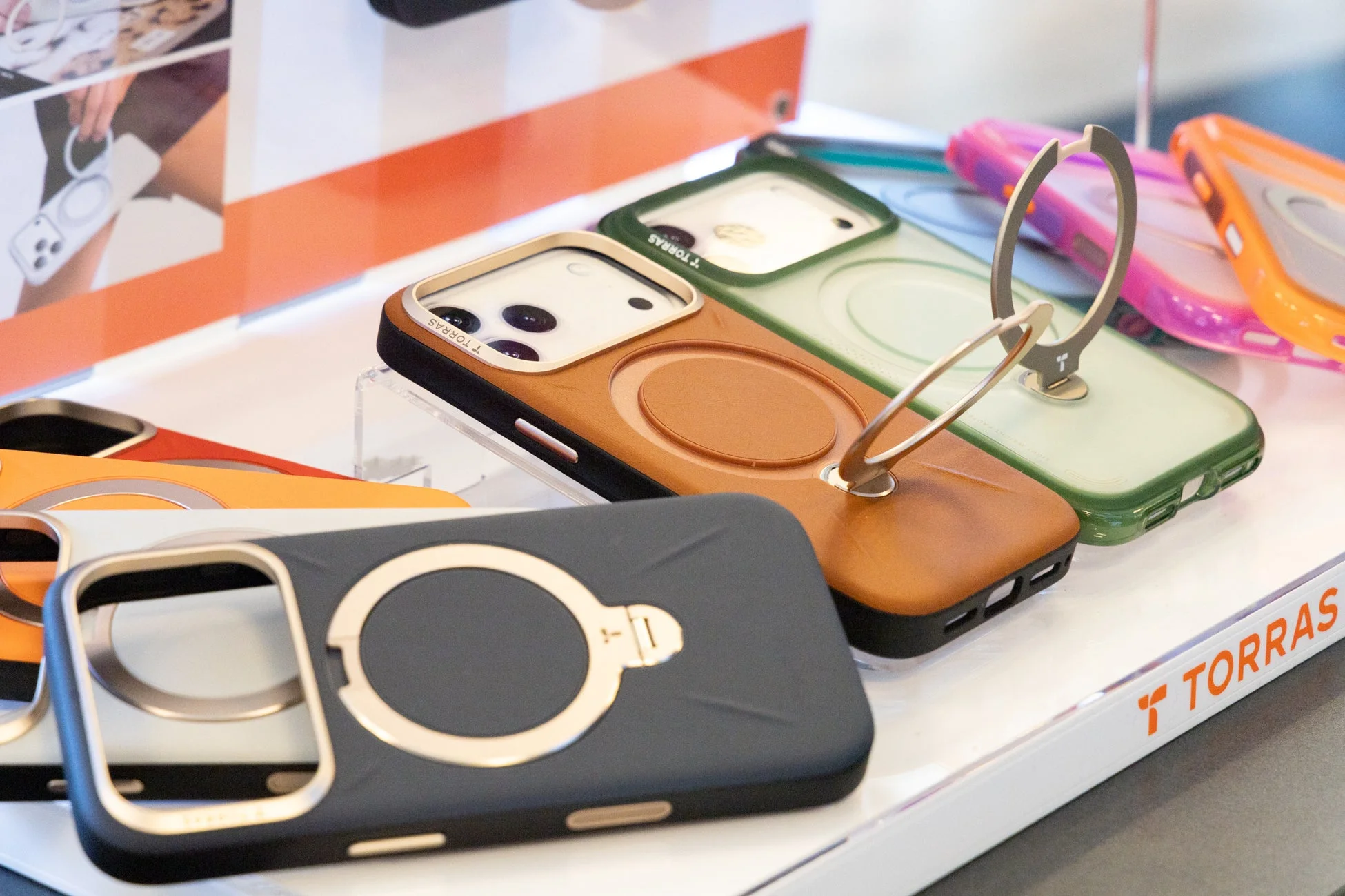 様々な色のスマートフォンケースが並べられた展示です。多くのケースにはリングスタンドが一体化されており、機能的なデザインが特徴です。