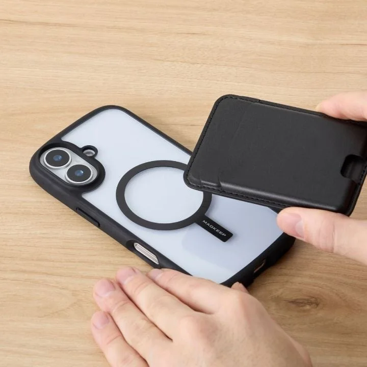 スマートフォンケースの背面にある磁気リングに、黒いウォレット型アクセサリーを装着しようとしている手元の様子。MagSafe対応のクリアケースと、その互換アクセサリーが写っています。