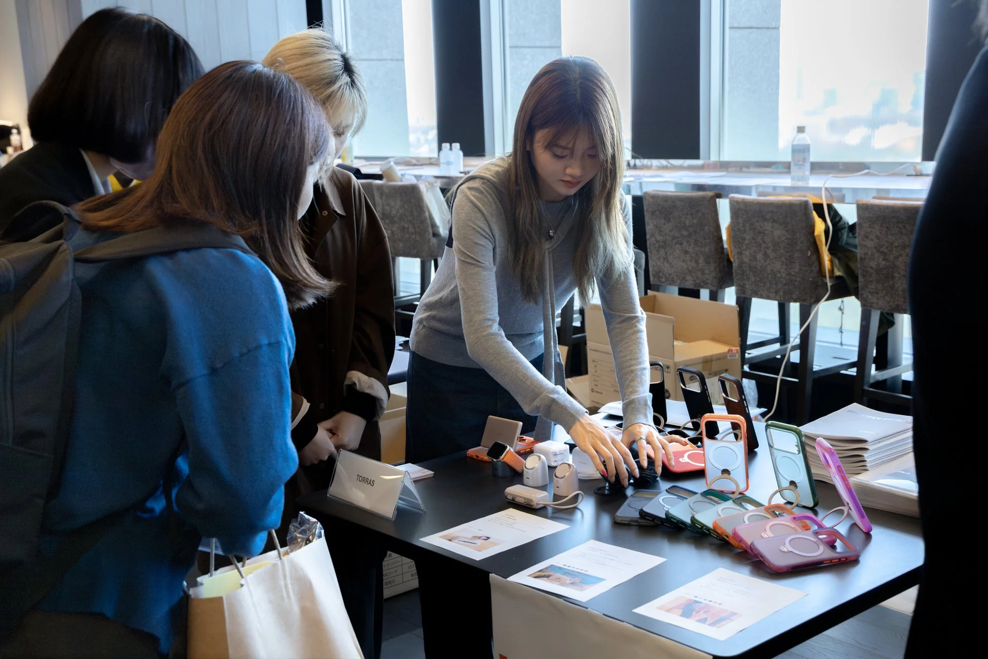 女性たちがスマートフォンケースやガジェットが並ぶブースで商品を見ている様子。