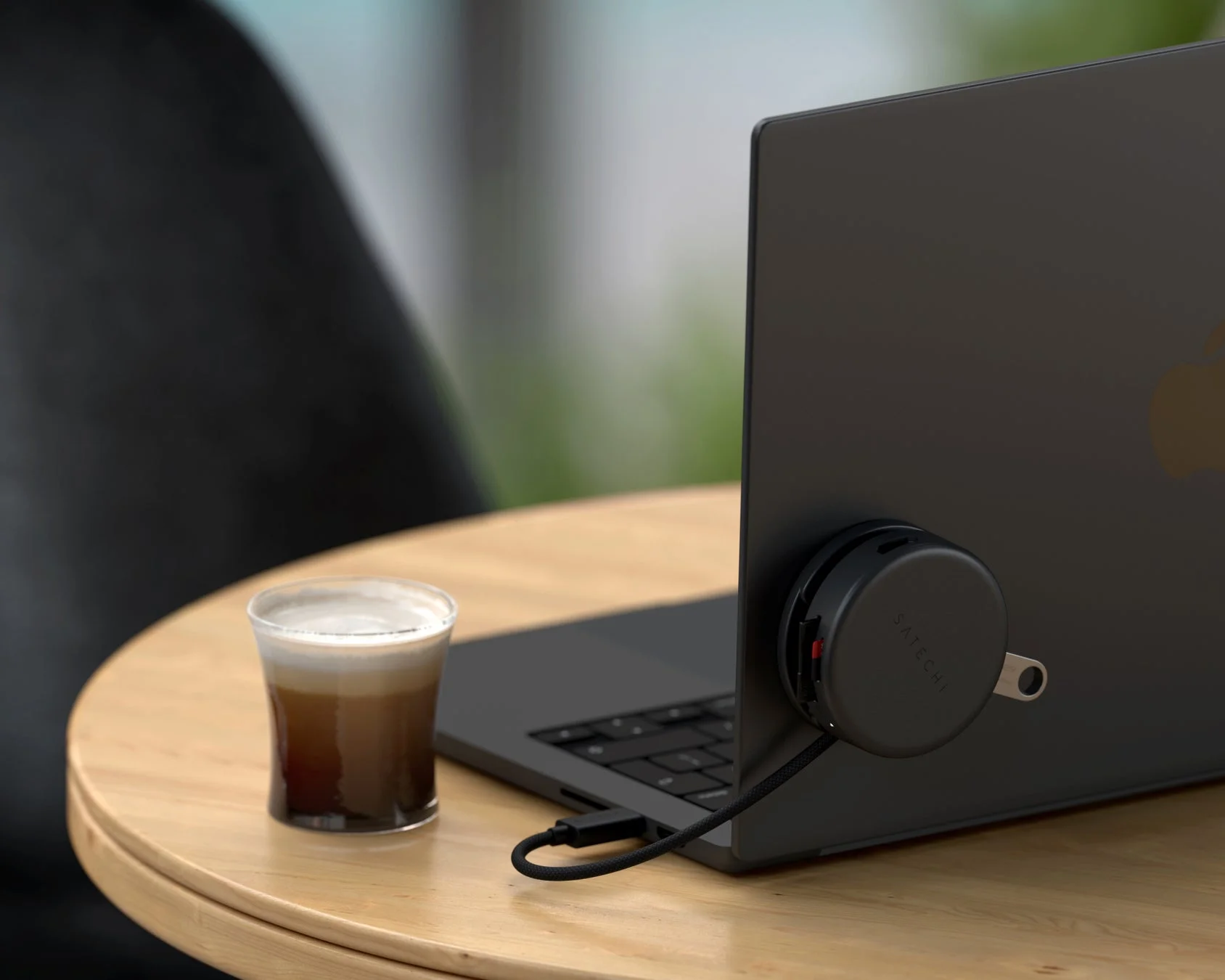 木製のテーブルに置かれた黒いラップトップの側面にSatechi製の丸いUSBハブが接続されています。