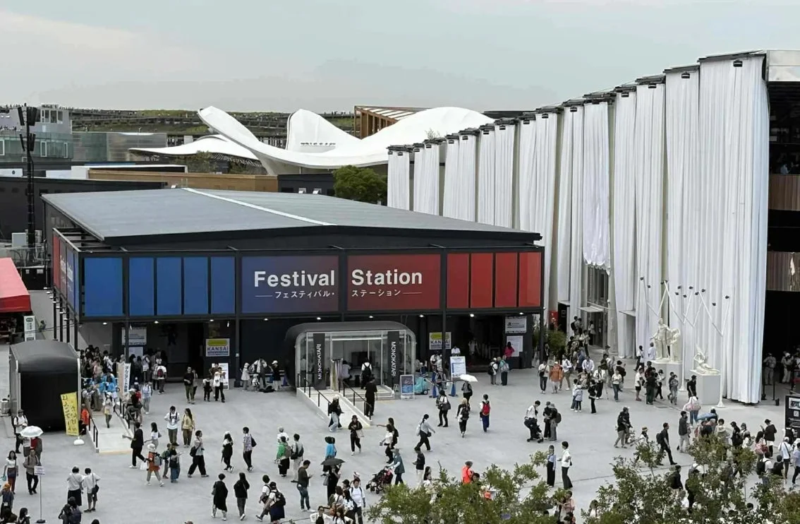 「Festival Station」と書かれた建物がある広々とした屋外イベントスペースで、多くの人々が行き交っています