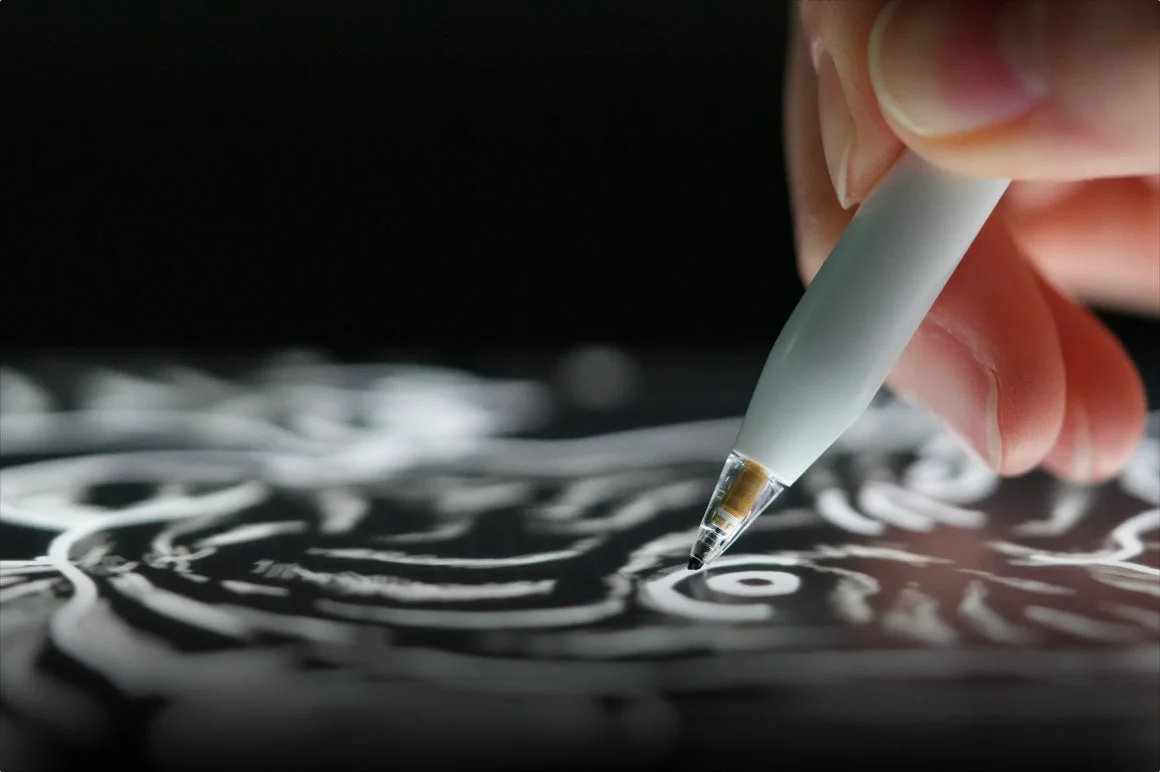 デジタルペンを使って、暗い画面に抽象的な白い模様を描いている手のクローズアップ。