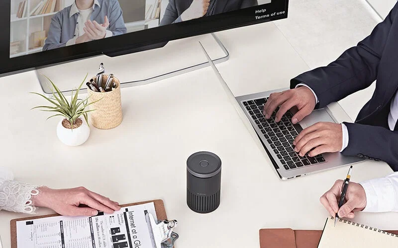 会議室でスピーカーフォンを囲んでWeb会議をする人々