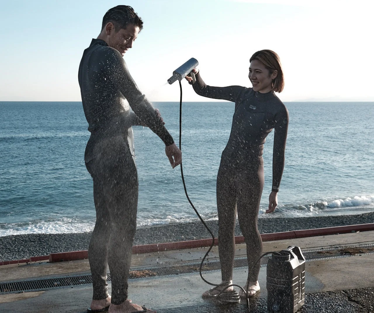 ウェットスーツ姿の男女がビーチでシャワーを楽しむ様子