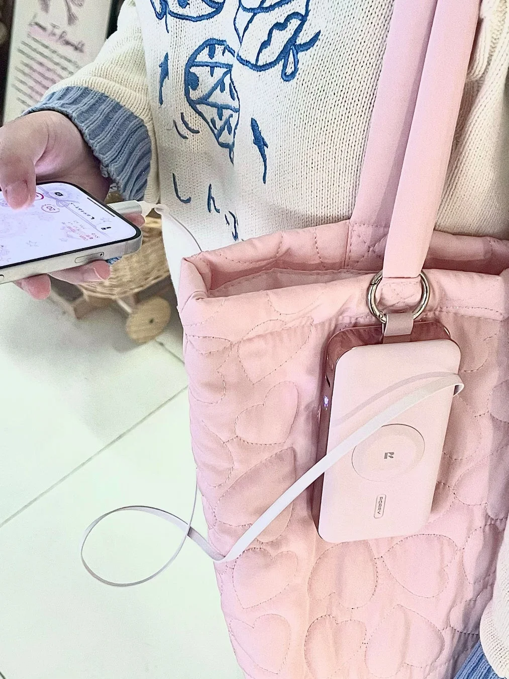 ピンクのキルティングトートバッグに装着されたピンクのモバイルバッテリーでiPhoneを充電している様子