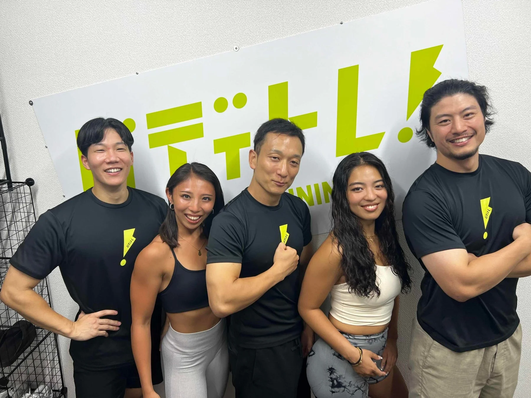 フィットネスジムで、笑顔の男女5人がスポーツウェア姿で並んでポーズをとっています。背景には「フィットレ!TRAINING」のロゴがあり、健康的な雰囲気が伝わります。