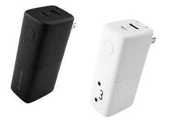 黒と白の2つのコンパクトなモバイルバッテリーが並んで写っています。それぞれUSBポートと折りたたみ式のACプラグを備え、黒い方には「ELECOM」のロゴ、白い方には顔のようなデザインがあります。スマートフォンなどの充電に便利な製品です。