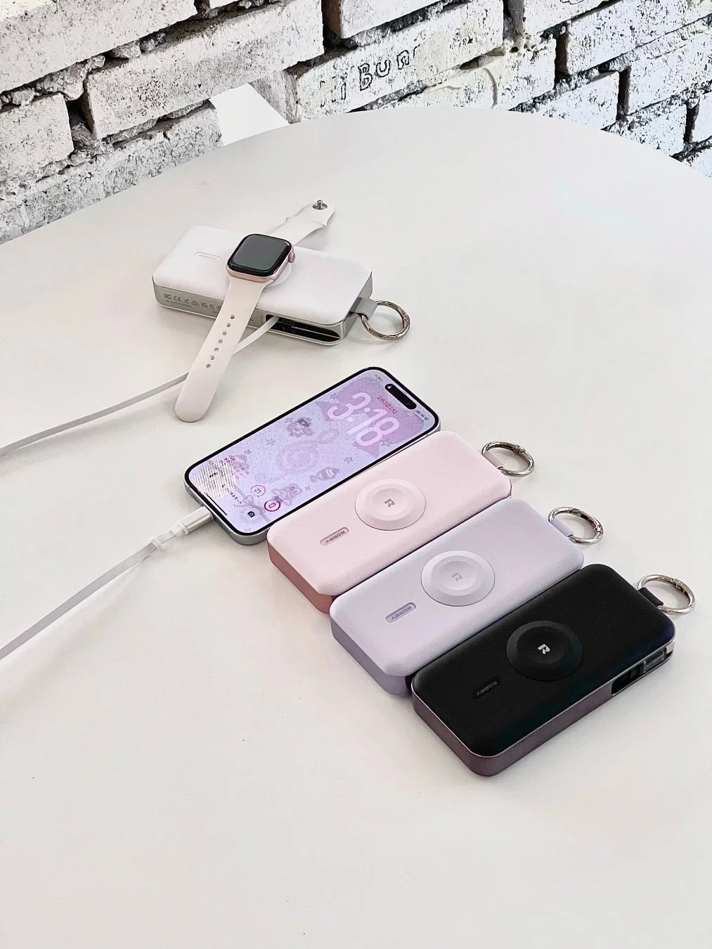 白いテーブルの上に、iPhone、Apple Watch、複数のモバイルバッテリーが並べられ、充電されている様子