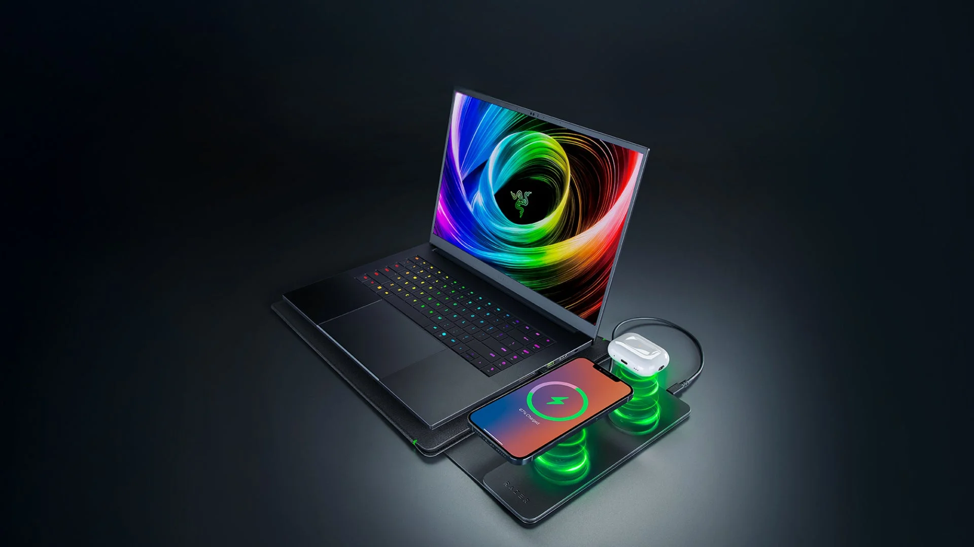 RazerノートPCの横でスマホとイヤホンがワイヤレス充電されている画像