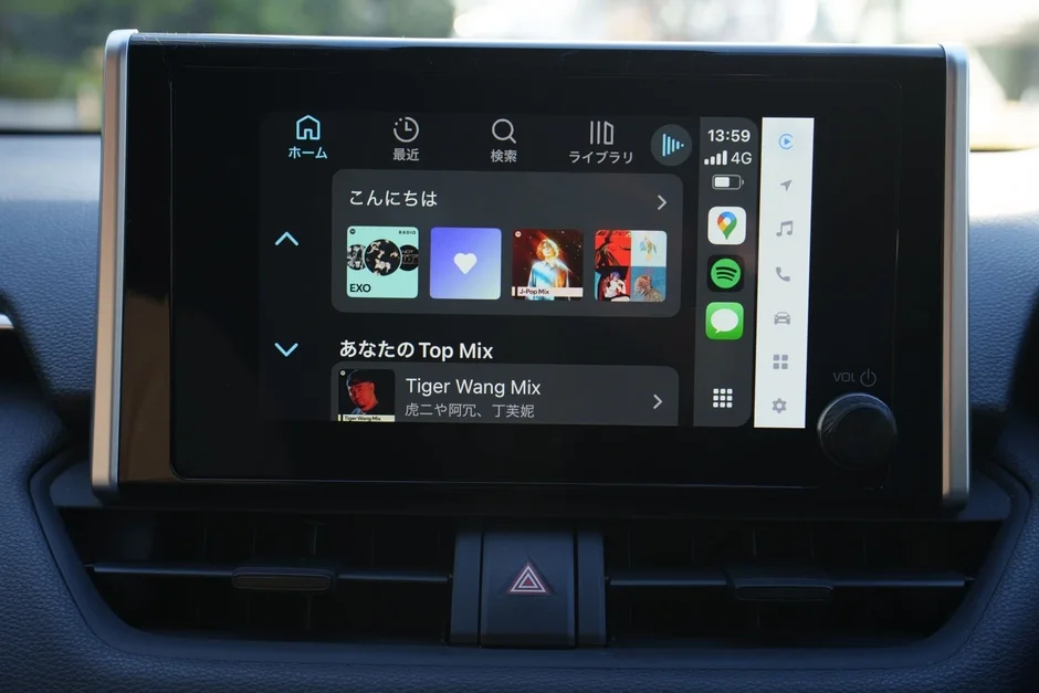 車のダッシュボードにあるインフォテイメントシステムの画面が映し出されています。音楽アプリのインターフェースが表示されており、再生中の楽曲やおすすめのプレイリスト、各種アプリのアイコンが見えます。時間や通信状況も確認できます。