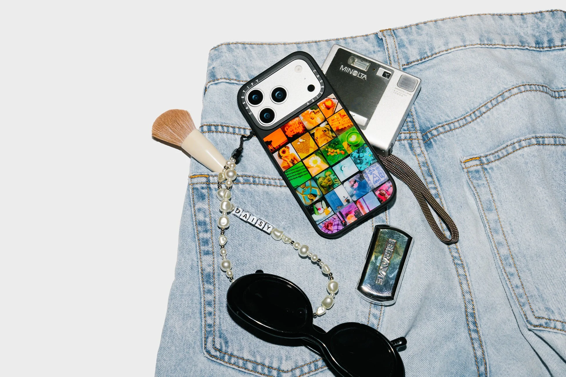 デニムの上に置かれたiPhoneとMINOLTAカメラ、サングラスなど