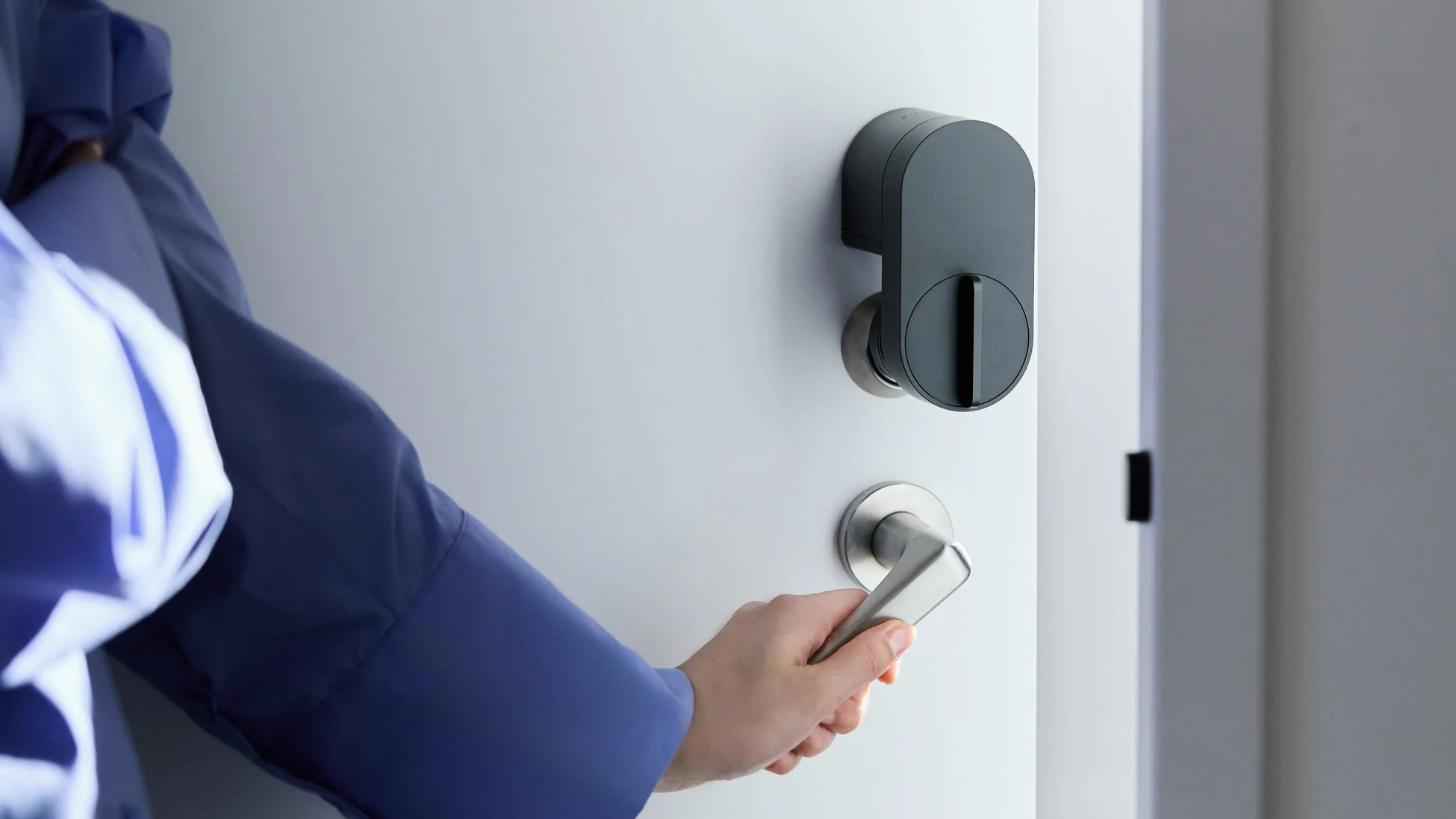 白いドアに設置されたスマートロックとドアノブを、青いシャツを着た人物の手が操作している