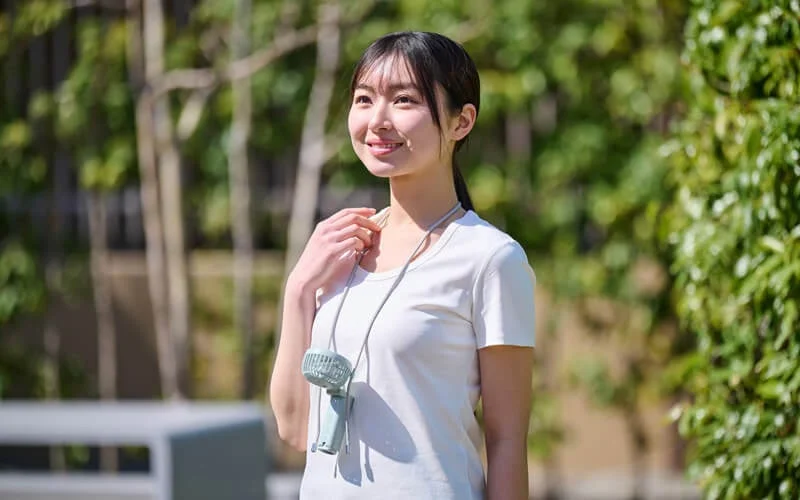 首掛け扇風機を身につけて屋外で笑顔を見せる女性