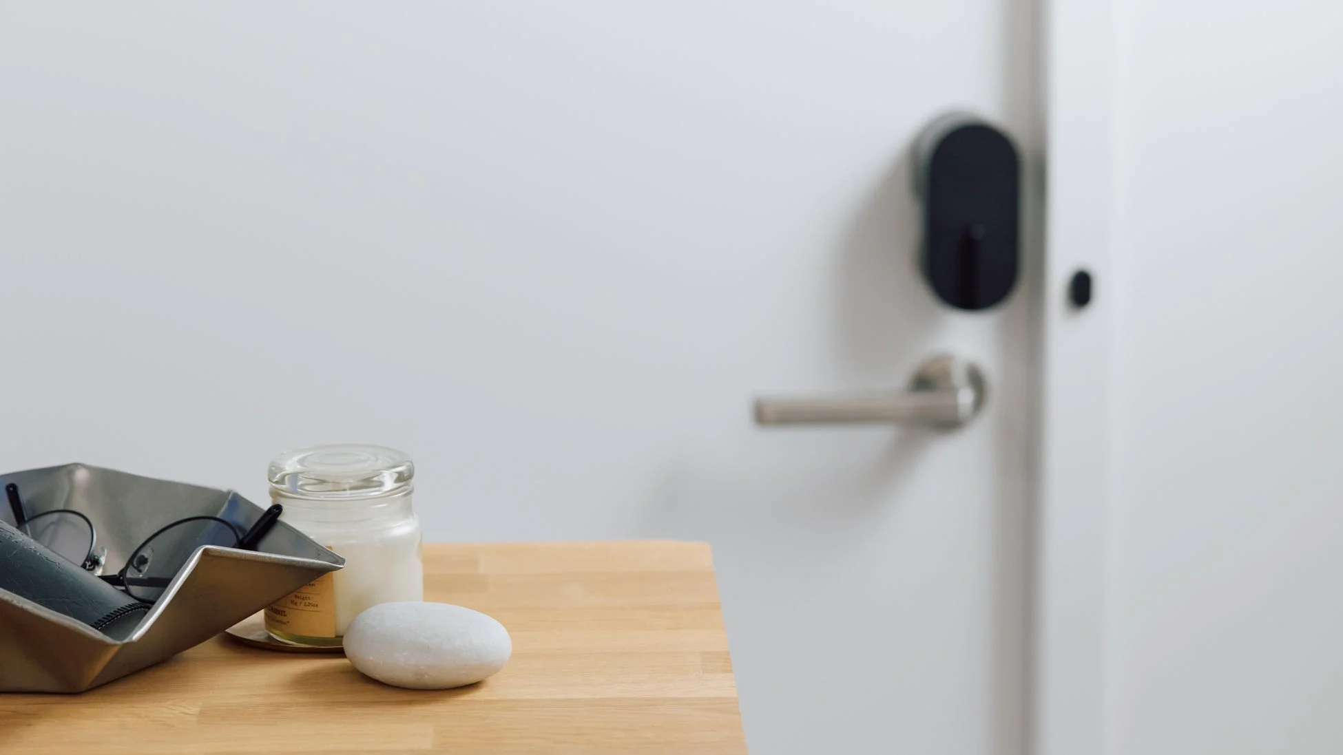 白いドアとスマートロックが背景にある木製テーブルに、メガネ、キャンドル、白い石が置かれている