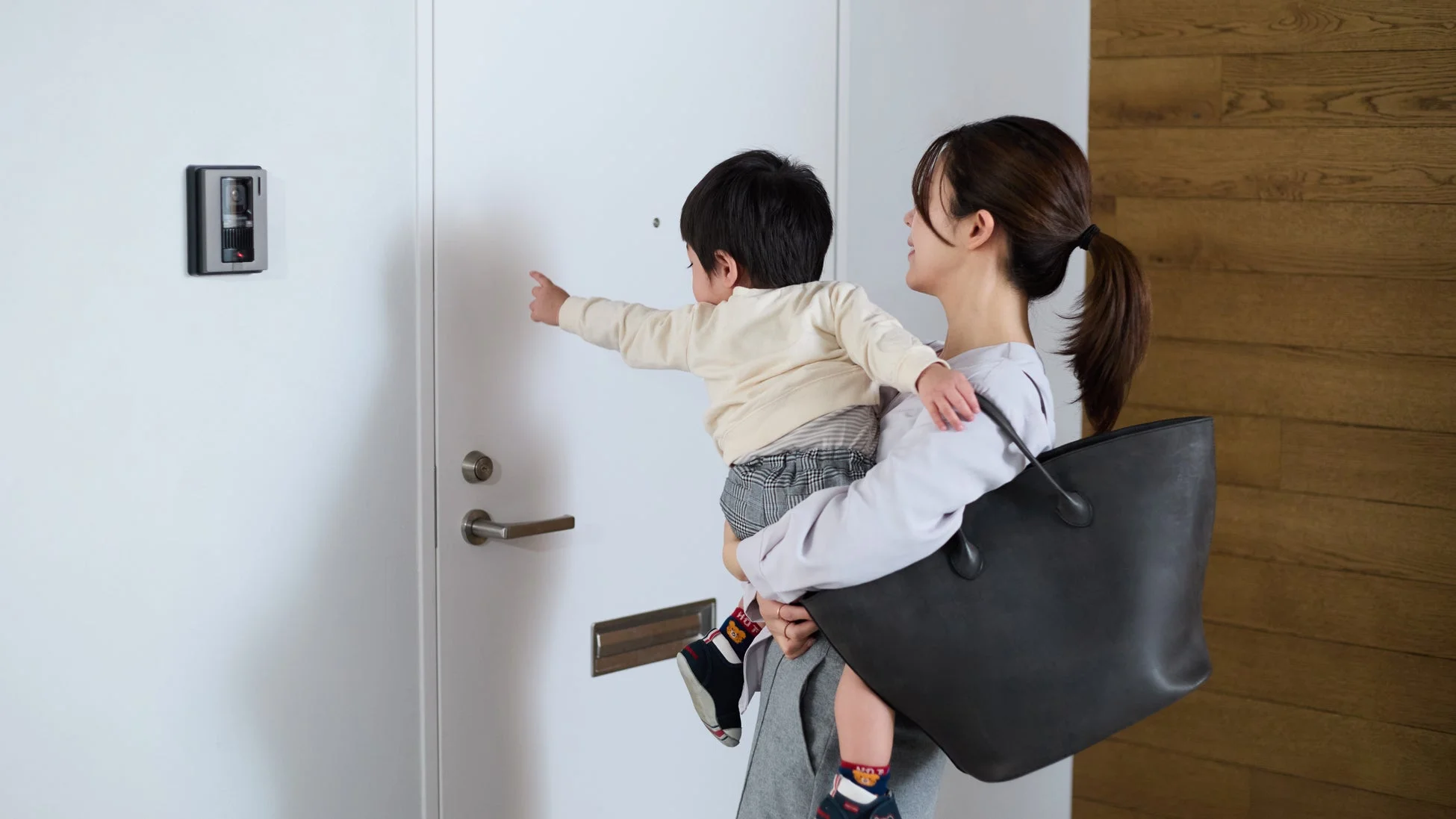 赤ちゃんを抱っこしている母親が玄関に立つ様子