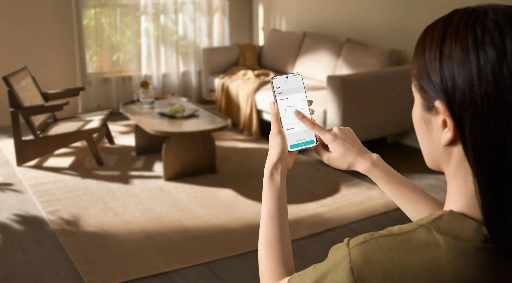 女性がリビングルームでスマートフォンを操作しており、画面にはグラフが表示されたアプリの設定画面が見えます。モダンなインテリアの中で、テクノロジーを活用した快適な生活を演出している様子がうかがえます。