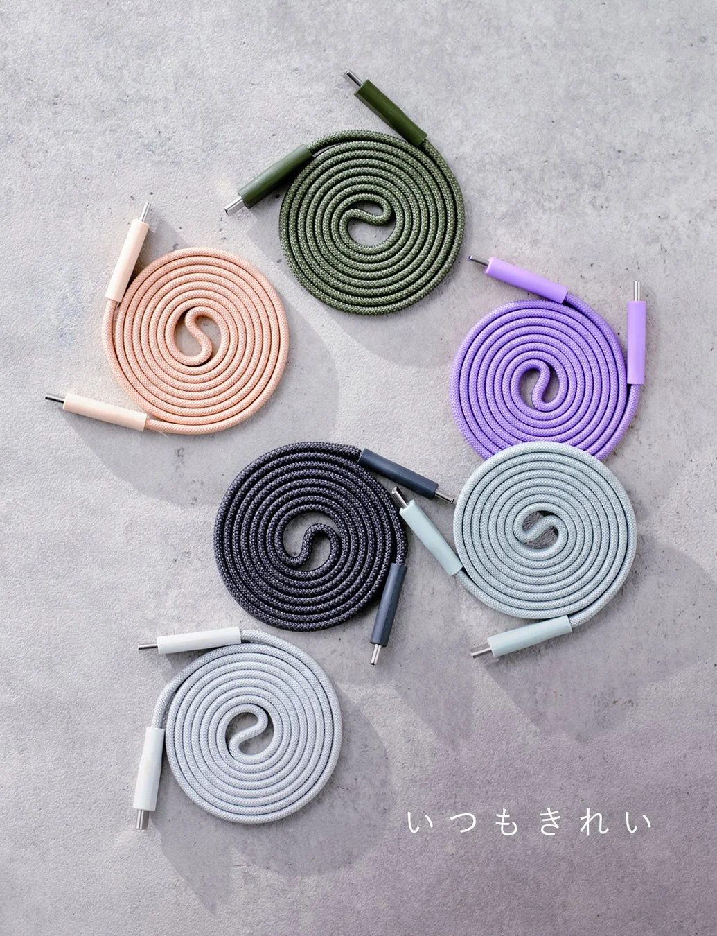 複数のカラフルな布巻きケーブルが、それぞれ渦巻き状にきれいにまとめられ、コンクリート調の背景に配置されています。