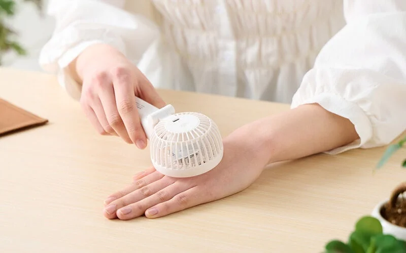 白い携帯扇風機で手のひらを冷やしている人物