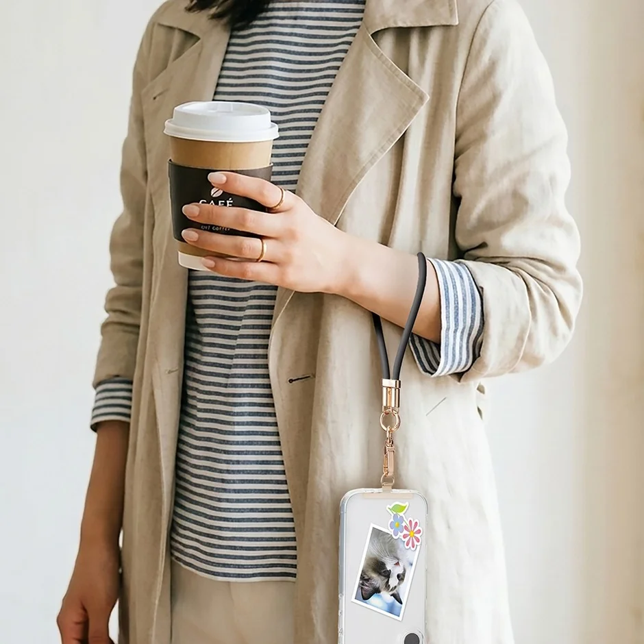 トレンチコートを着た女性がコーヒーカップと手首にストラップをつけたスマートフォンを持っている様子
