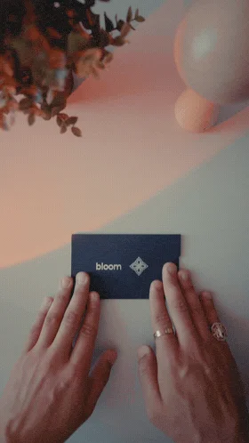 両手が「bloom」とロゴが書かれた紺色のカードを丁寧に持っている様子。