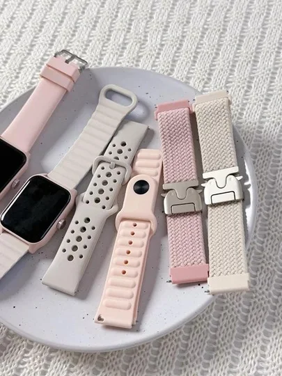 パステルピンクやベージュのスマートウォッチバンドが複数、白い皿の上に置かれています。シリコン製や布製など、様々な素材とデザインのバンドが見られ、腕時計のカスタマイズを提案しているようです。