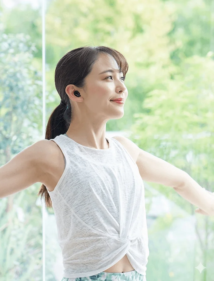窓辺でヨガをする女性がワイヤレスイヤホンを装着している様子