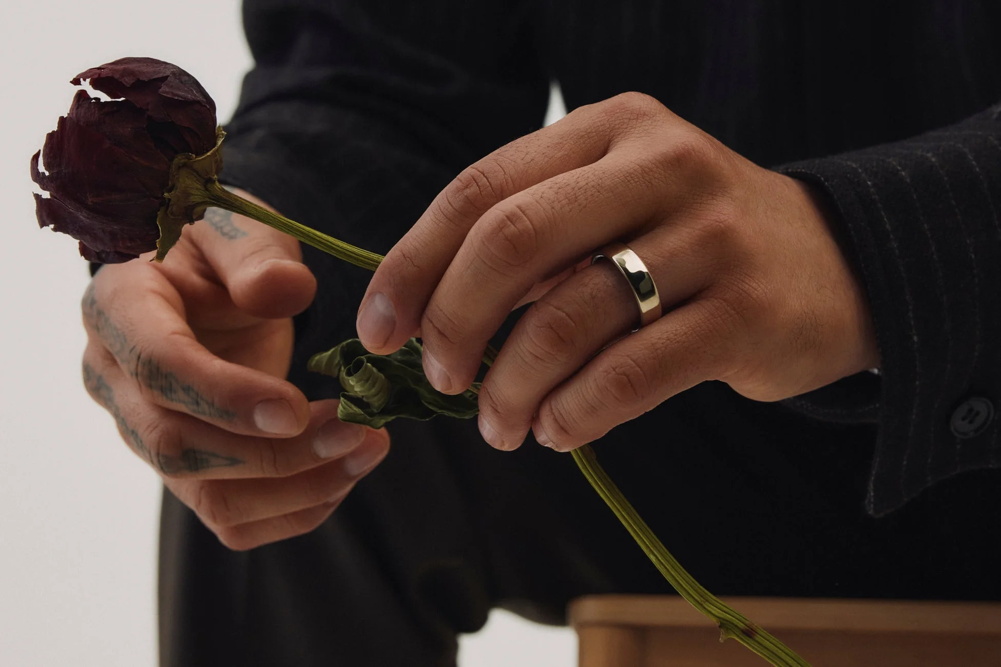 指輪をはめた手が、しおれた深紅のバラの茎を優しく持っている様子