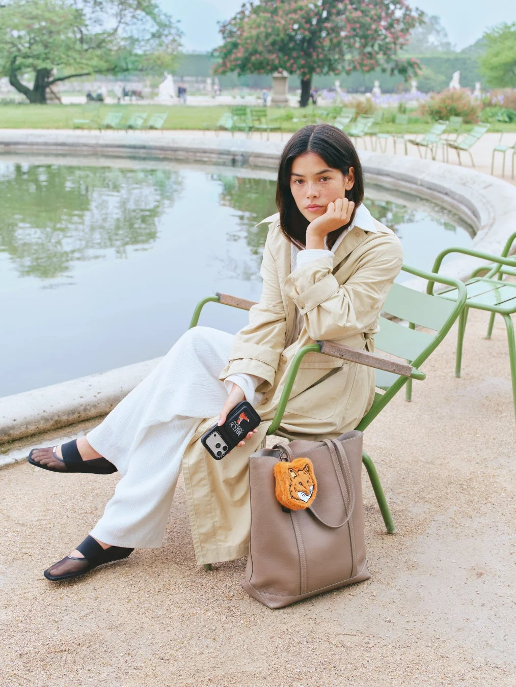 公園でリラックスする女性。キツネのチャームが付いたトートバッグとスマートフォンを持っています。