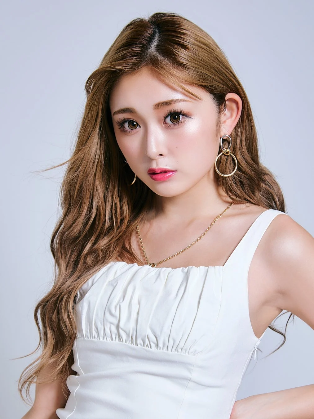 白いトップスを着用し、長い茶色の髪と魅力的なメイクが特徴の女性のポートレートです。