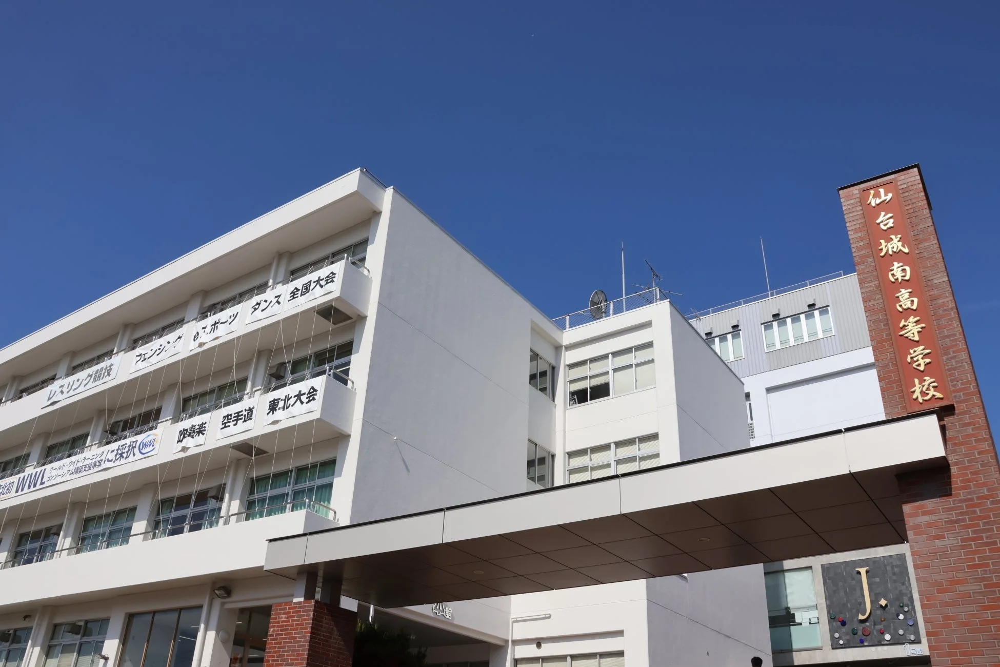 青空の下、仙台城南高等学校の校舎が写っており、全国大会や東北大会への出場、グローバル・ワイド・ラーニング採択などのクラブ活動の成果を示す横断幕が掲げられています。